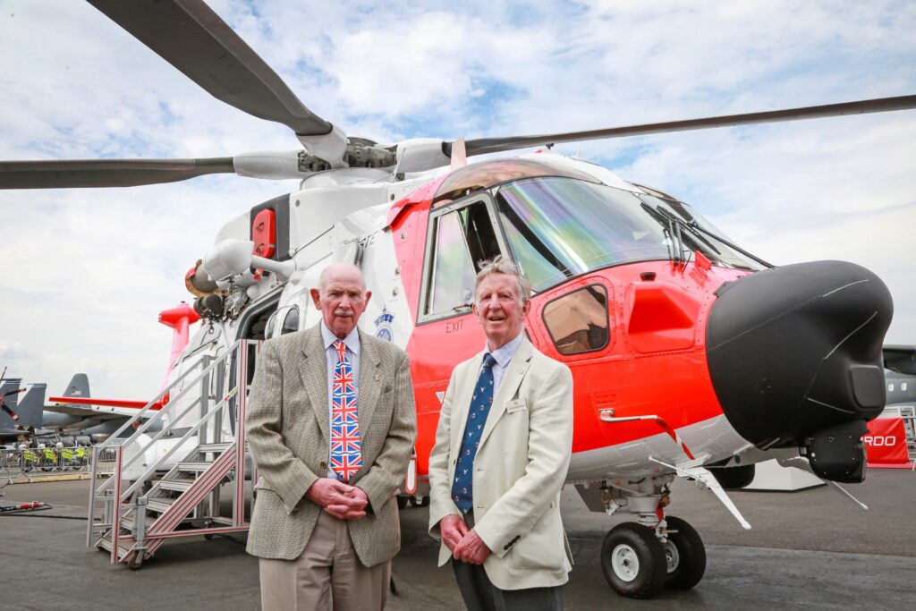 Barnbrook systems managing director Tony Barnett (L) and Sir Donald Spiers, then chairman of Farnborough Aerospace Consortium (R) at the 2018 Farnborough International Airshow in front of a helicopter with Barnbrook System's fuel switch
