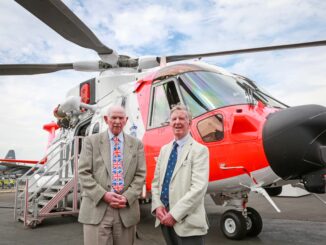 Barnbrook systems managing director Tony Barnett (L) and Sir Donald Spiers, then chairman of Farnborough Aerospace Consortium (R) at the 2018 Farnborough International Airshow in front of a helicopter with Barnbrook System's fuel switch
