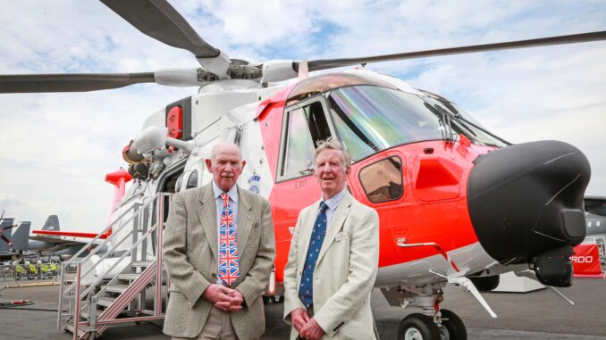 Barnbrook systems managing director Tony Barnett (L) and Sir Donald Spiers, then chairman of Farnborough Aerospace Consortium (R) at the 2018 Farnborough International Airshow in front of a helicopter with Barnbrook System's fuel switch